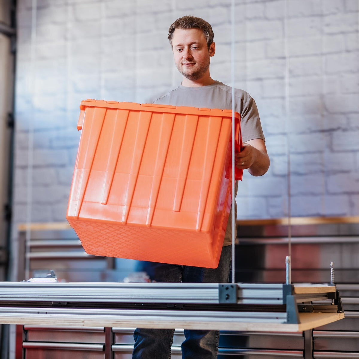 A person loading a storage tote onto the Auxx Attic-Lift platform at standing height